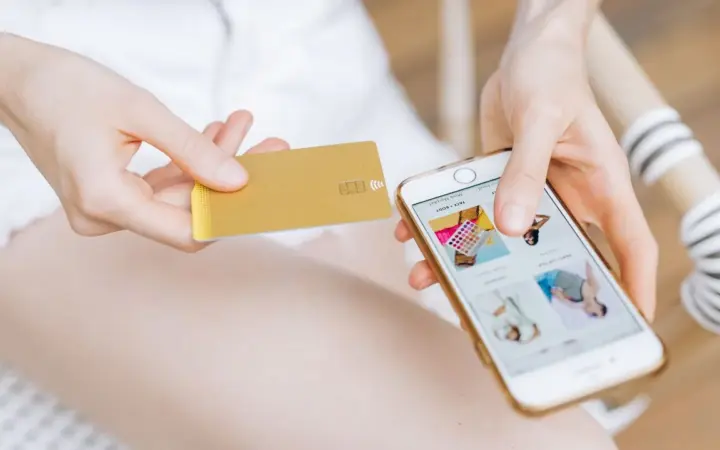 Pessoa segurando um celular e cartão enquanto faz uma compra online