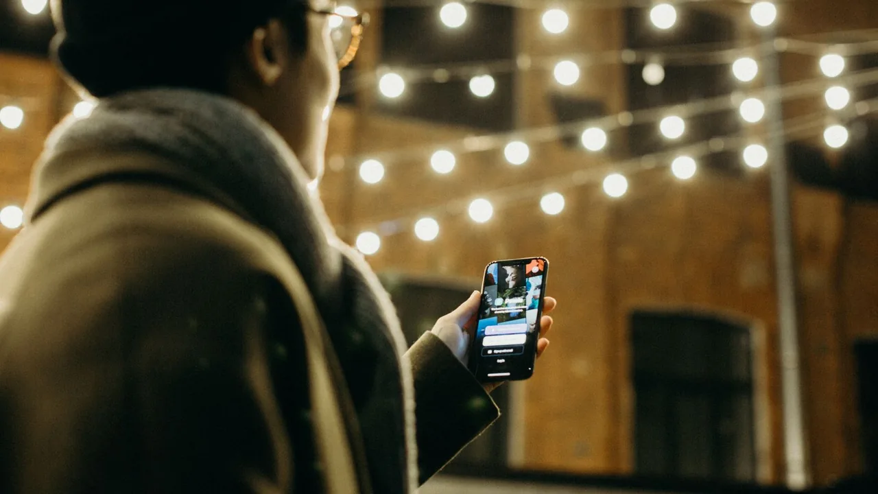 Pessoa usando um smartphone ao lado de um computador, exemplo de câmera de celular para videochamadas