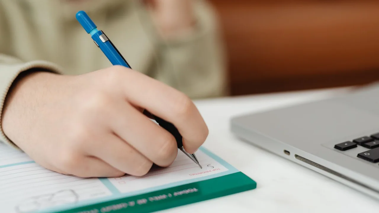 Pessoa preenchendo um formulário ao lado de um laptop