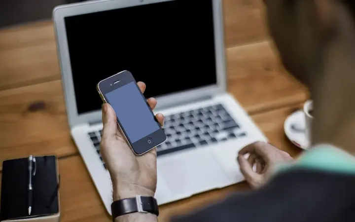 Pessoa usando smartphone e notebook para organizar o atendimento de clientes pelo WhatsApp Business