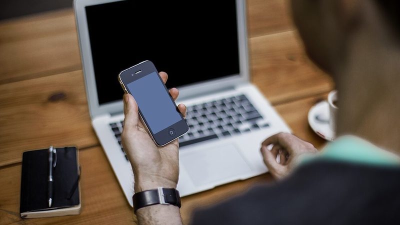 Pessoa usando smartphone e notebook para organizar atendimento no WhatsApp Business