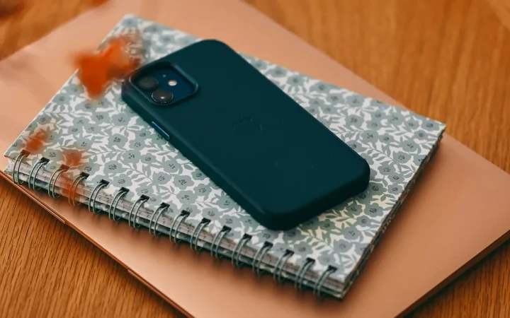 Smartphone sobre caderno ao lado de um computador portátil