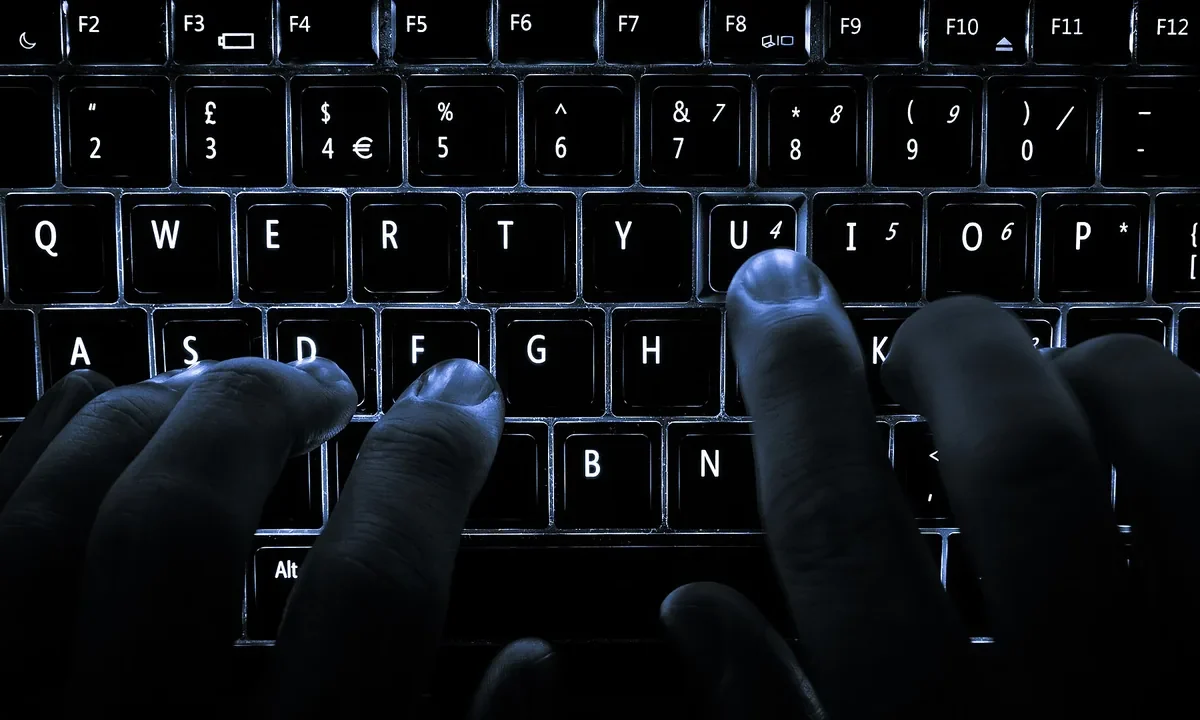 Mãos digitando em um teclado de notebook iluminado