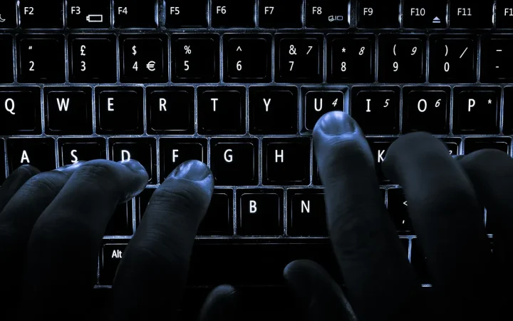 Mãos digitando em um teclado de notebook iluminado