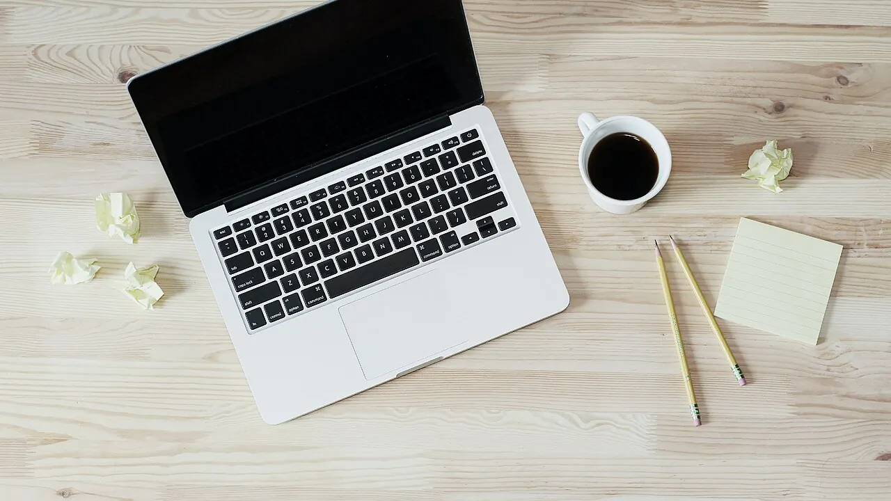 Notebook aberto sobre uma mesa de trabalho com café e bloco de notas