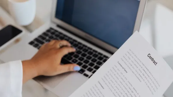Pessoa revisando um contrato ao lado de um laptop