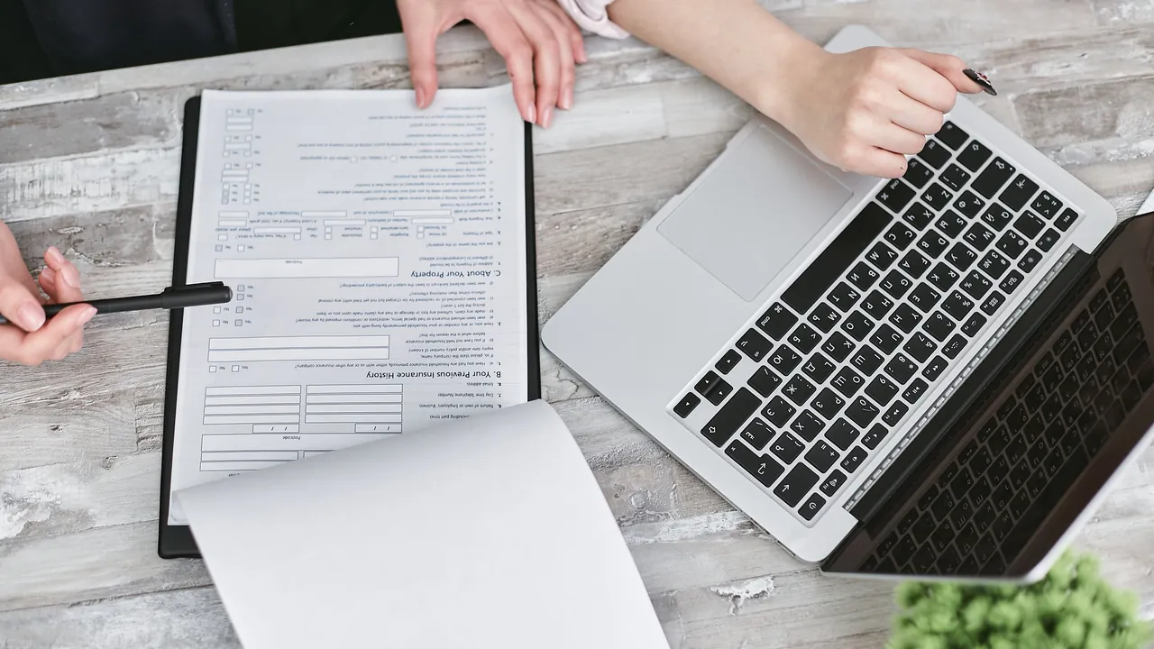 Pessoa trabalhando com documentos e notebook sobre uma mesa