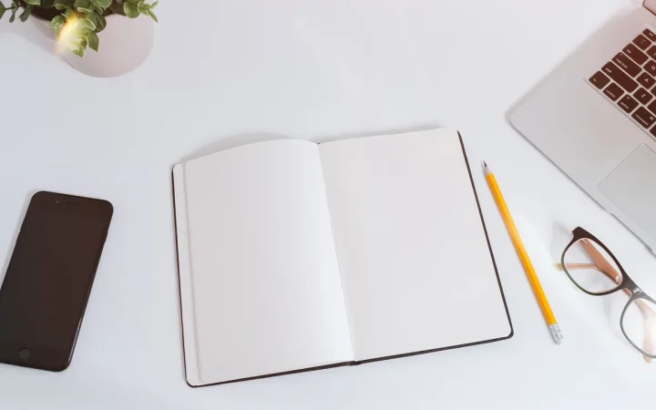 Mesa de trabalho com caderno, celular e laptop, representando a organização de dados em uma planilha