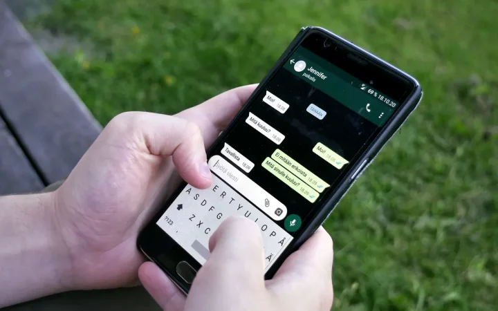 Pessoa segura um celular com uma conversa do WhatsApp aberta ao ar livre.