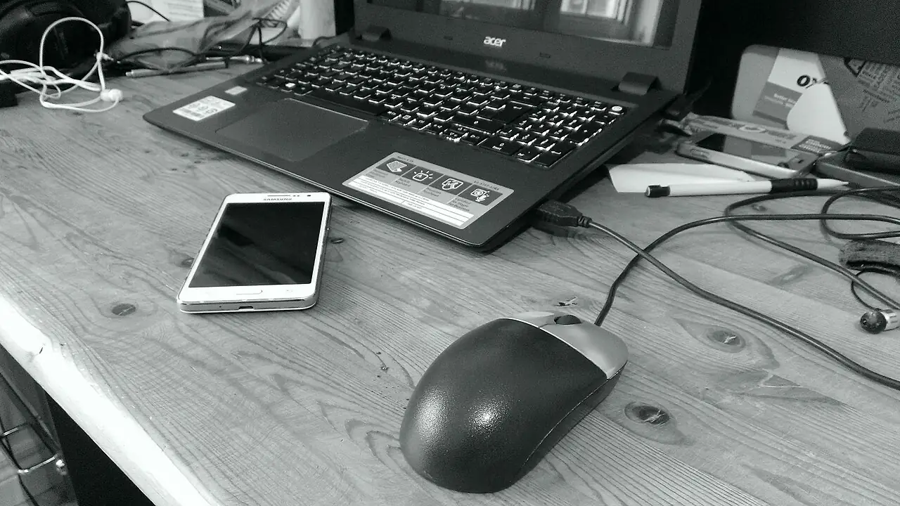 Notebook, celular e mouse sobre uma mesa de trabalho