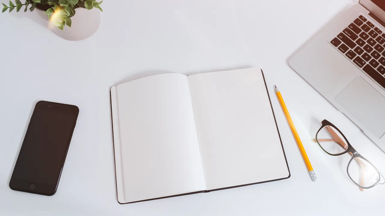 Caderno aberto, celular e notebook sobre uma mesa, representando a organização de dados